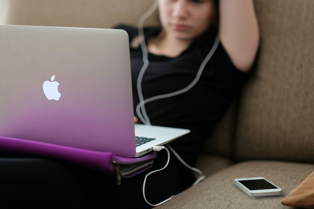 Imagem de capa do texto sobre procrastinação e ansiedade. Na foto, uma mulher usando o notebook no sofá com um celular ao lado.